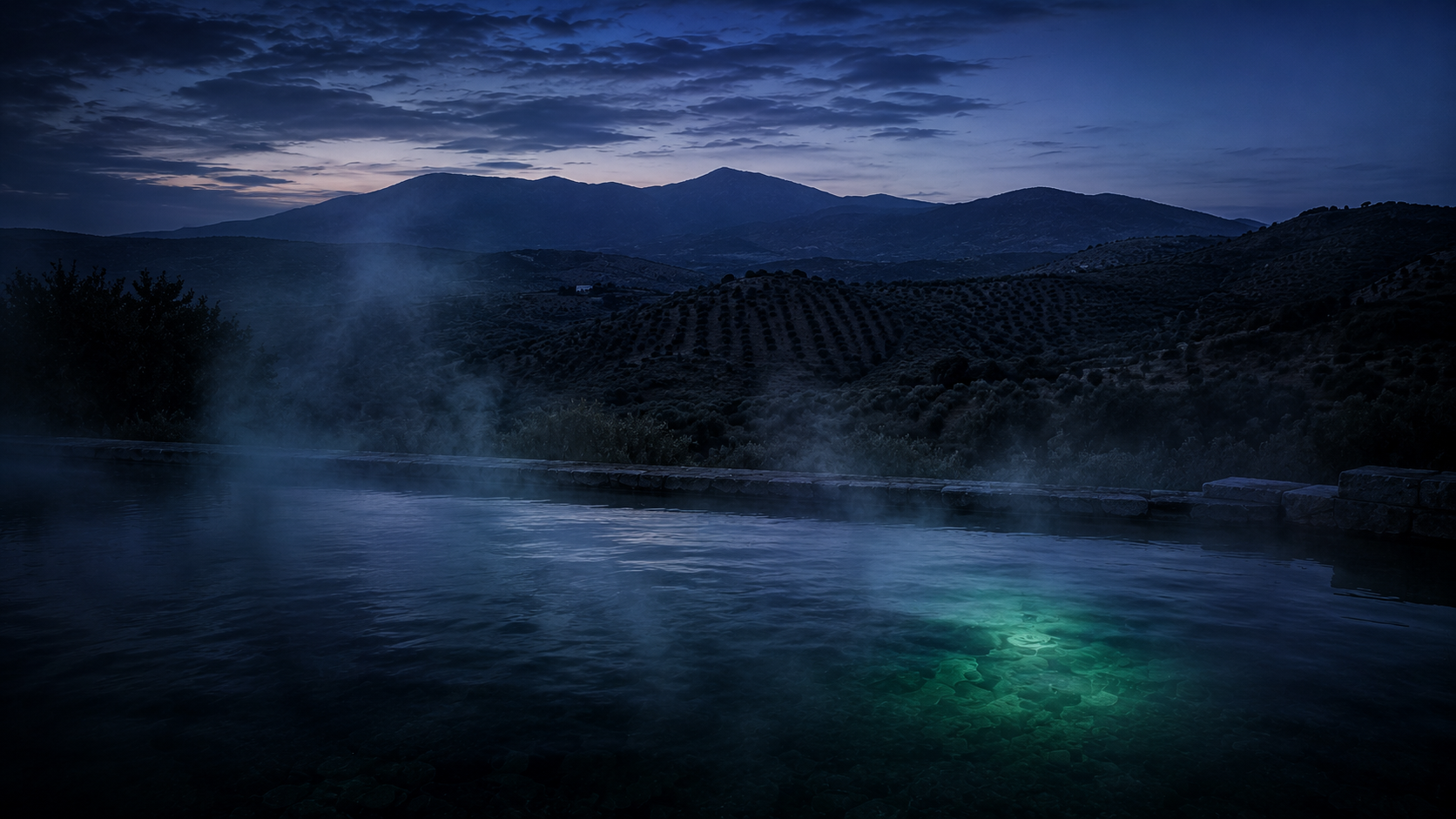 Piscina termal exterior con vapor frente a un paisaje de sierra andaluza al anochecer