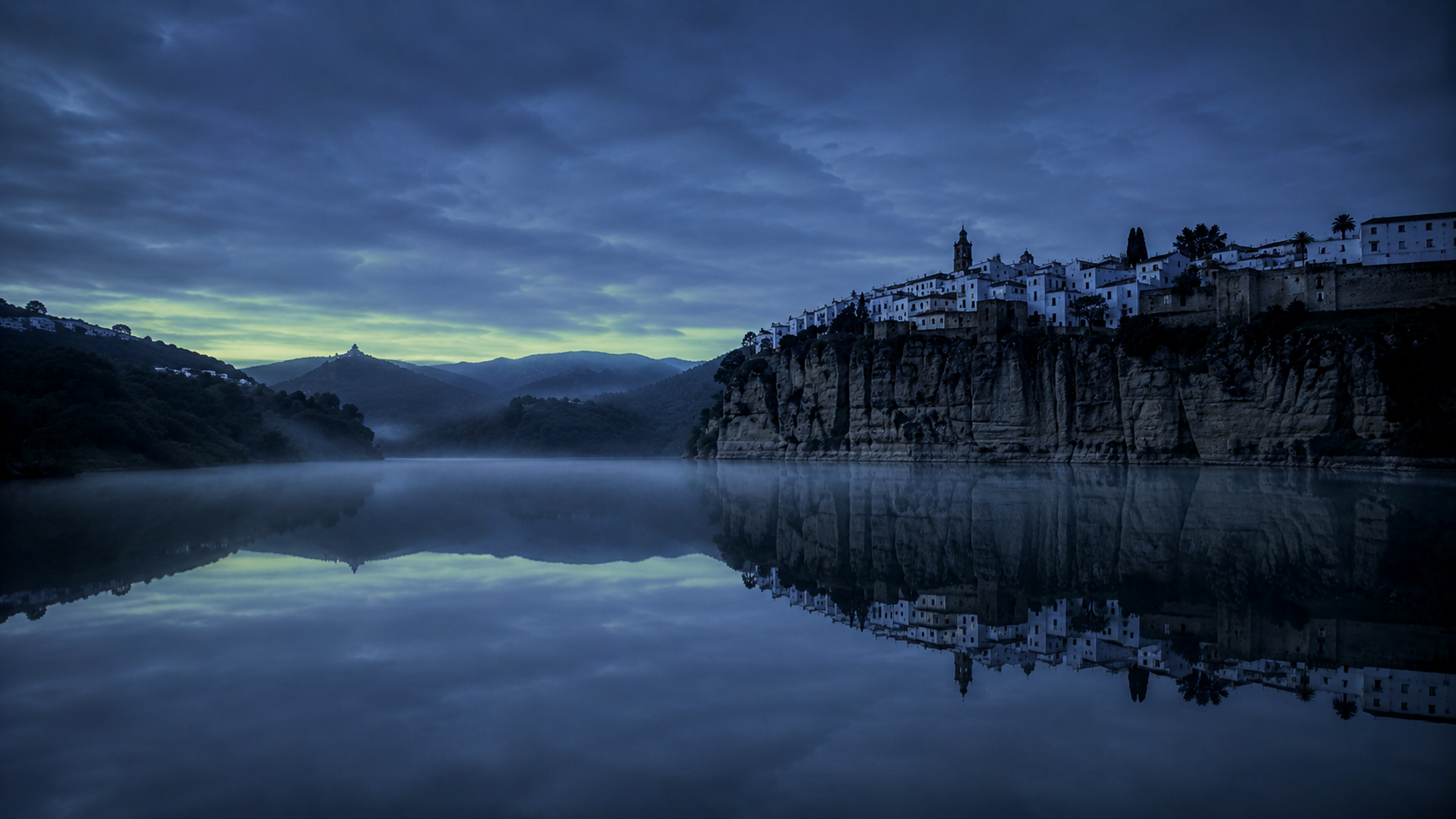 El embalse de Arcos al anochecer con el pueblo blanco iluminado reflejado en el agua