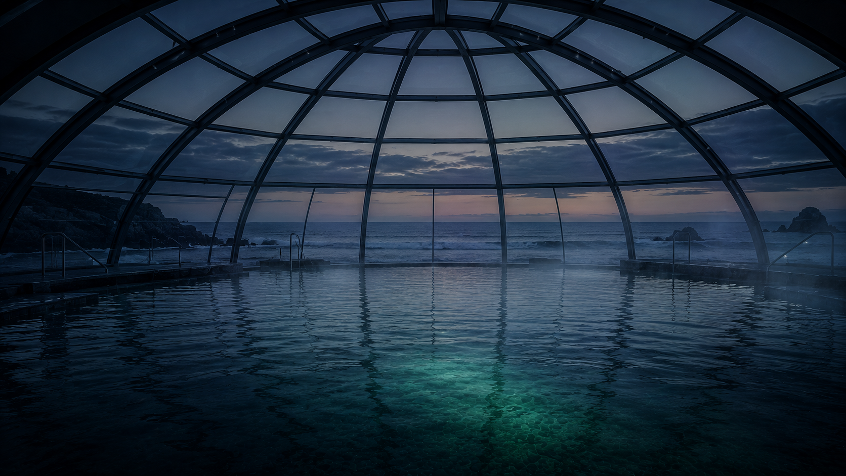 Gran piscina de agua de mar bajo una cúpula de cristal con vistas al océano al anochecer