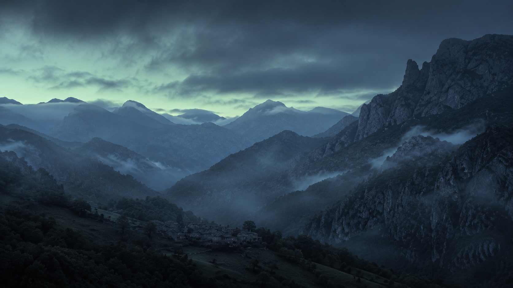 Los Picos de Europa al amanecer azul, con niebla baja sobre los prados del valle