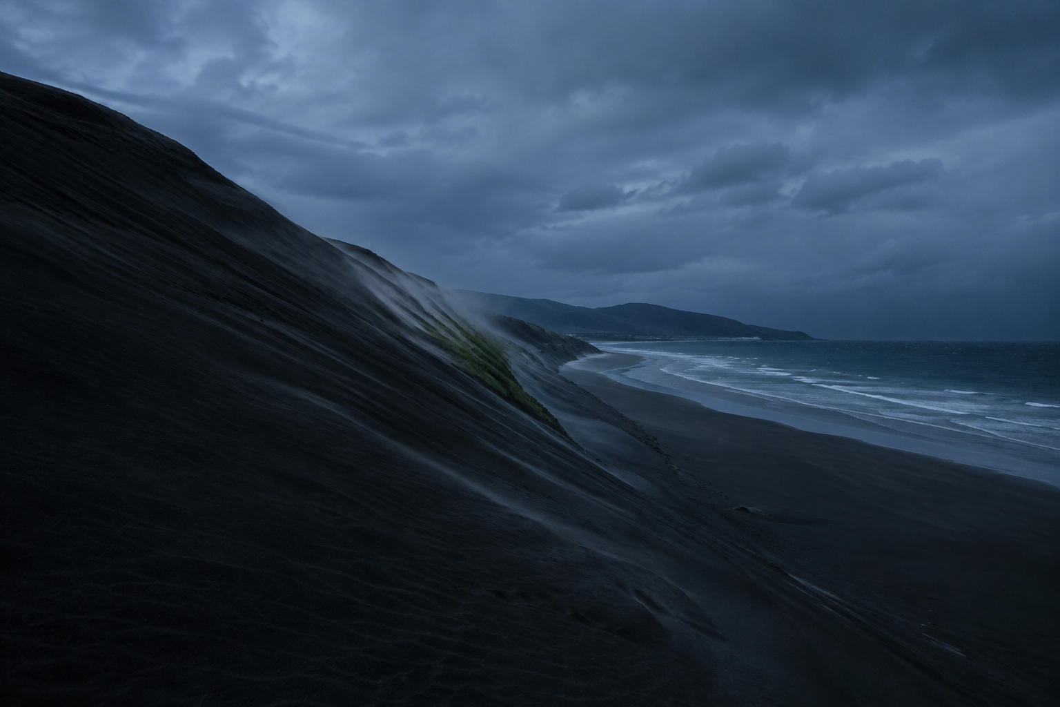 La duna de Valdevaqueros barrida por el viento a la hora azul, con la arena levantándose en la cresta y sin nadie a la vista