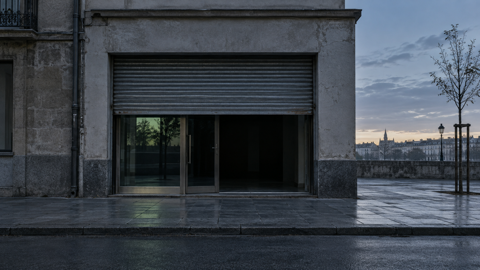 Fachada de un local con la persiana medio subida al amanecer y una luz verde tenue reflejada en el cristal