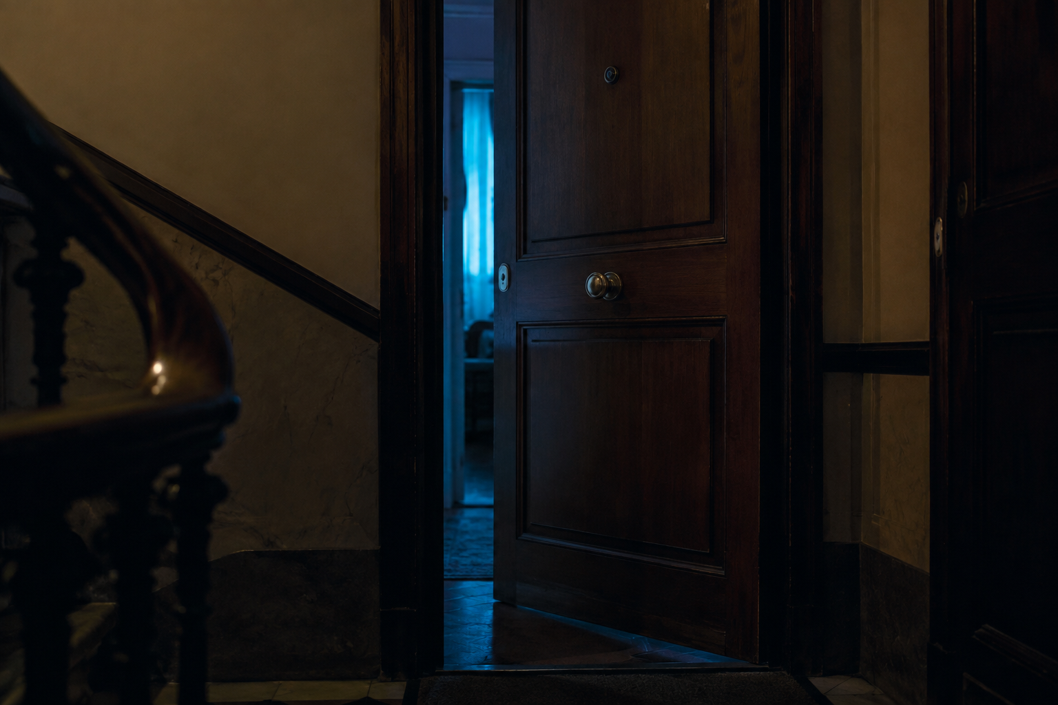 Puerta de madera de un piso antiguo entreabierta, con luz azul saliendo del interior hacia un rellano en penumbra
