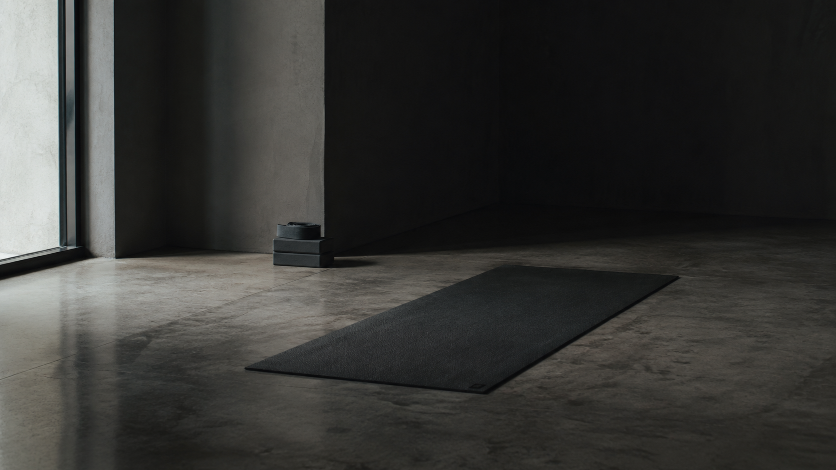 Esterilla de yoga desplegada y vacía sobre suelo de hormigón pulido, iluminada por una luz fría lateral