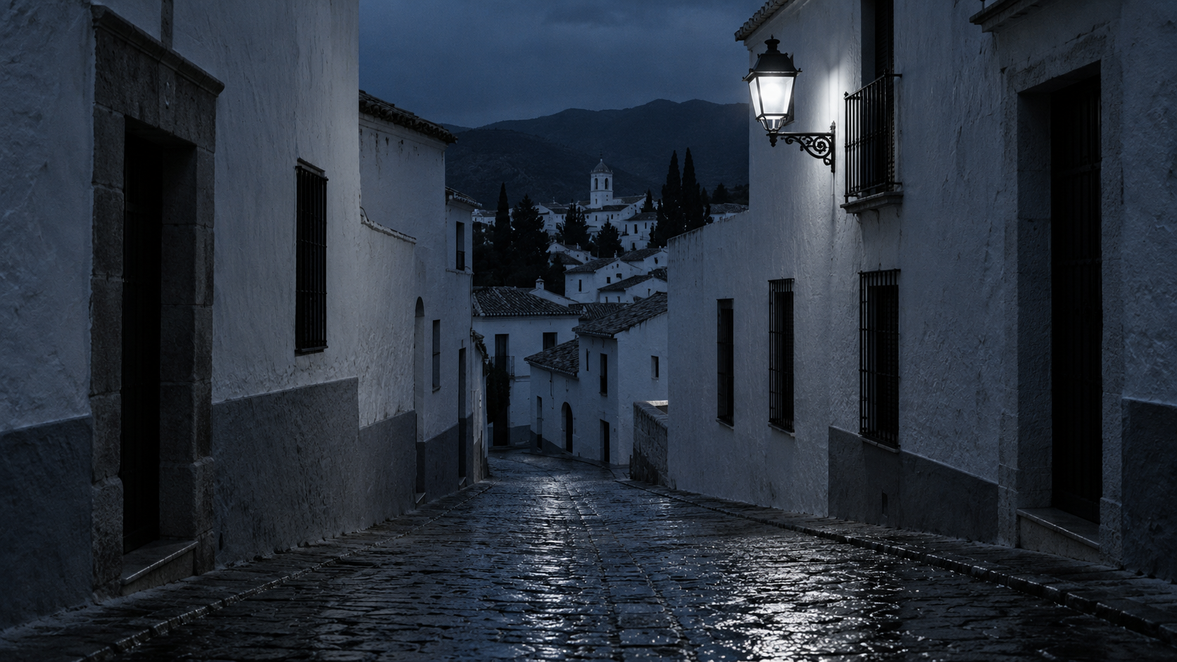 Calle estrecha de casco antiguo andaluz en la hora azul, con las persianas bajadas y la luz de una farola sobre el empedrado