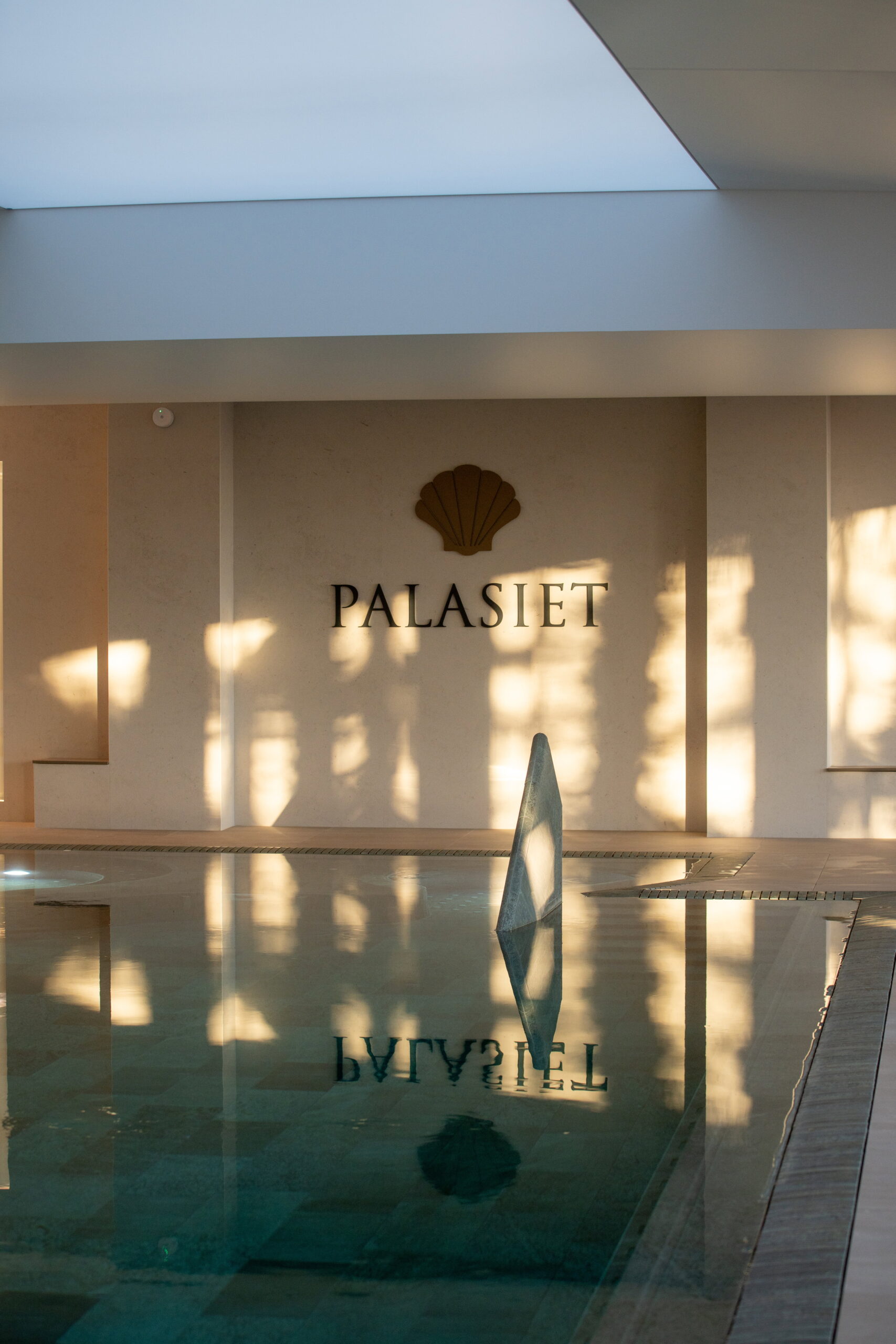 Piscina interior de Palasiet con el nombre de la casa en la pared, reflejado en el agua con luz dorada