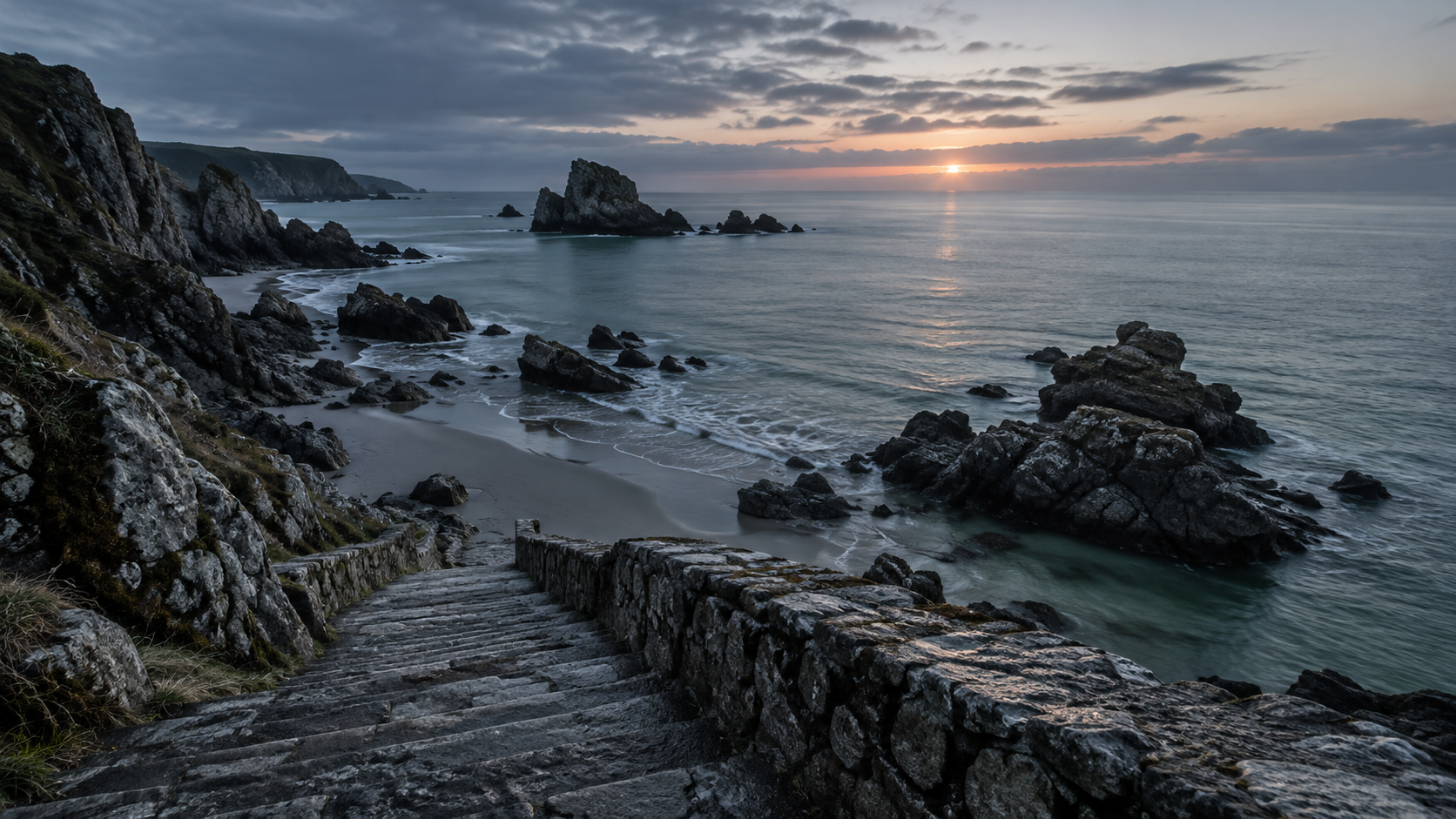 Mar de invierno al amanecer en una playa del Cantábrico, con escalera de piedra hacia el agua y nadie a la vista
